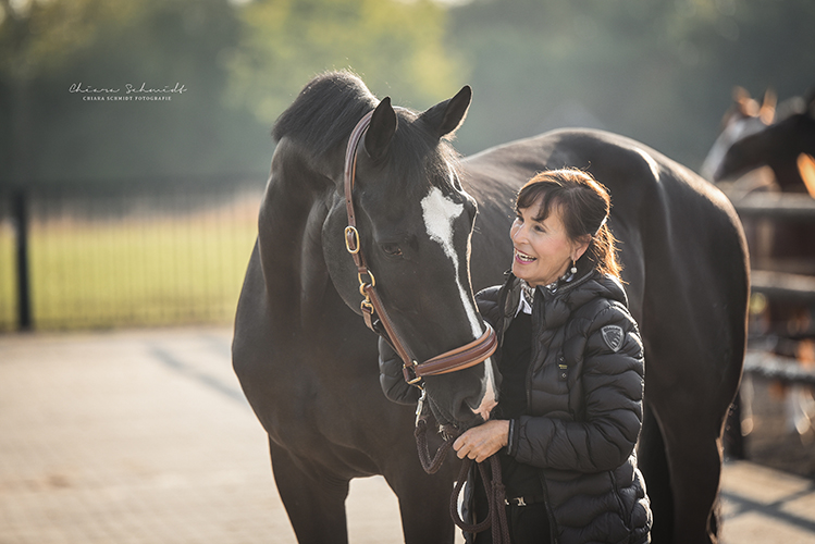 Frau steht neben einem Pferd und lächelt es an