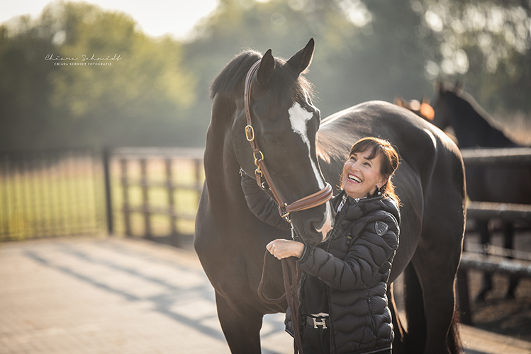 Frau steht neben einem Pferd und lächelt es an